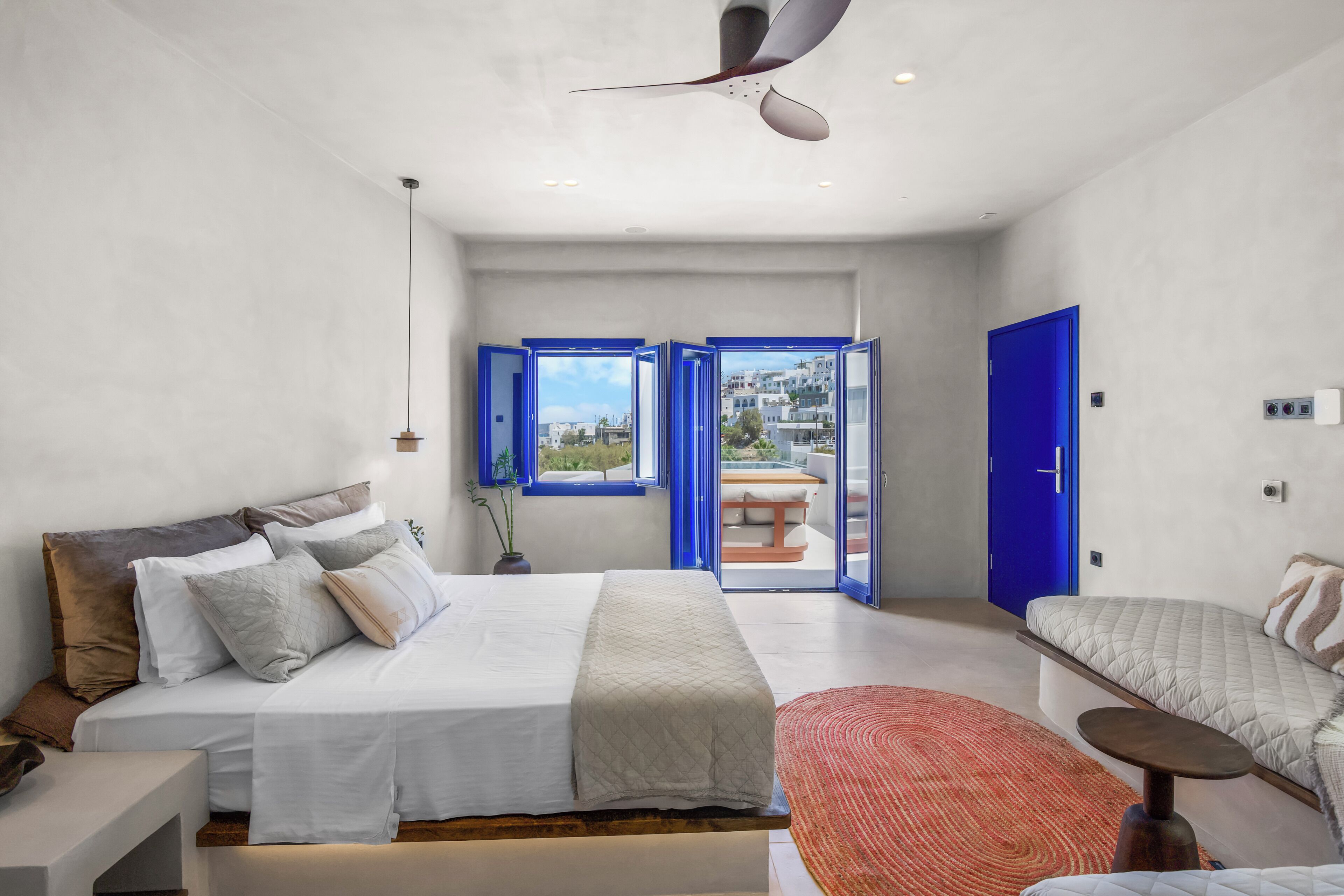 A modern bedroom with a bed, a seating area, and a view through a door.