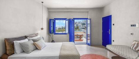 A modern bedroom with a bed, a seating area, and a view through a door.