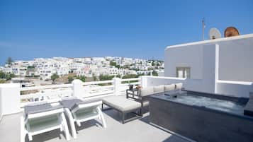 A rooftop terrace with white furniture, a hot tub, and a view of a white-washed town.