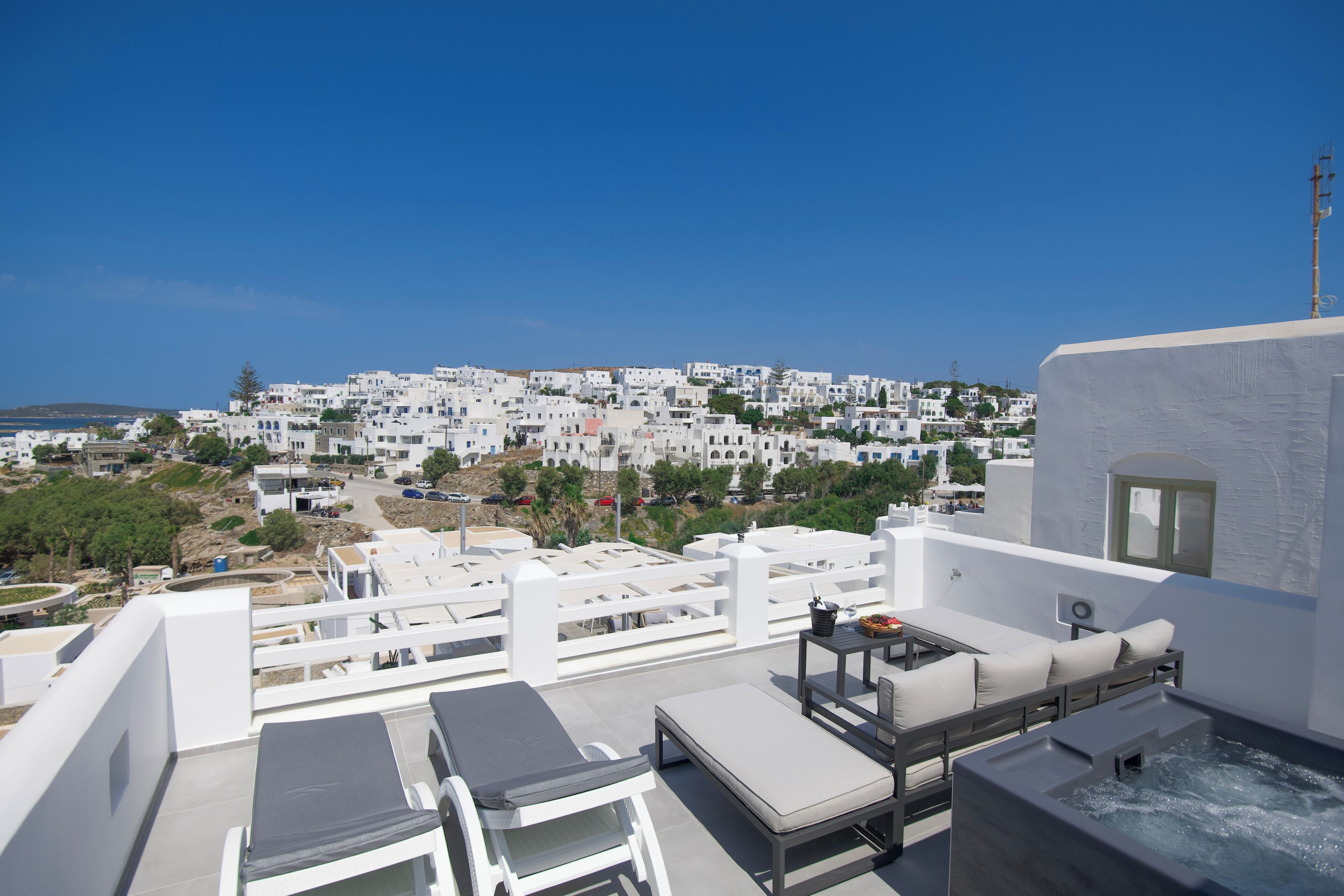 A rooftop terrace with lounge chairs, a hot tub, and a view of a white-washed town.