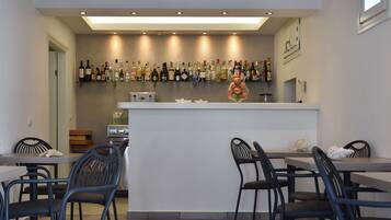 Un área de bar moderna con una encimera blanca, varios estantes con botellas de licores y un adorno colgante decorativo.