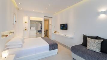 A modern bedroom with a large bed, a smaller sofa, a walk-in closet, and a TV on the wall.