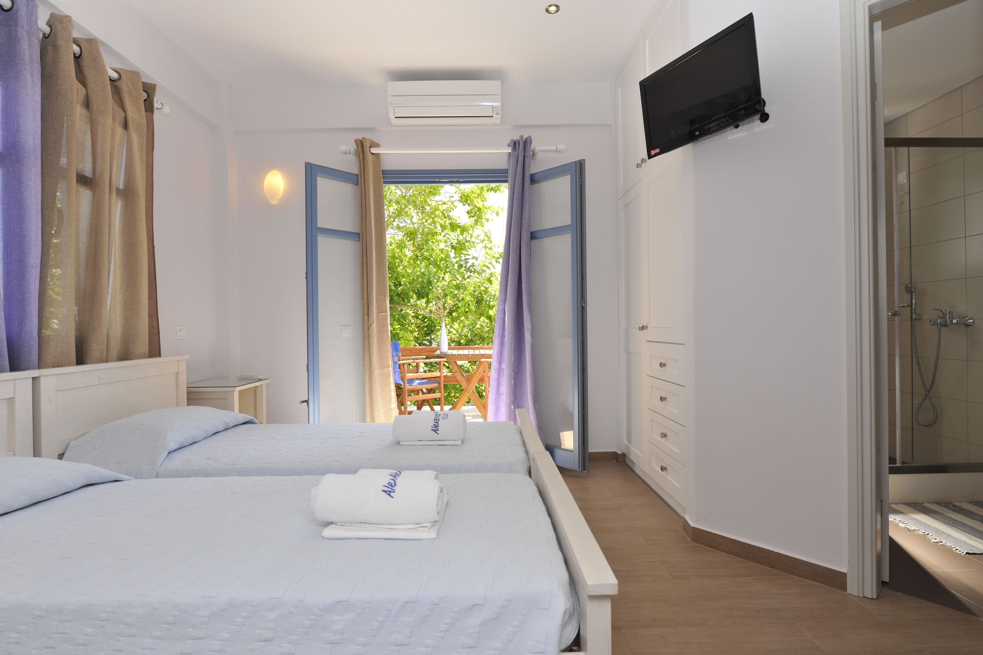A bedroom with two beds, a TV mounted on the wall, and a shower area.