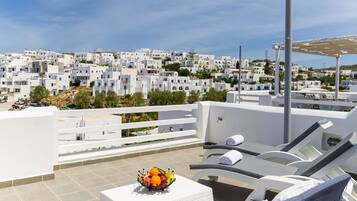 A rooftop terrace with white furniture, a fruit bowl, and a view of white buildings in the background.