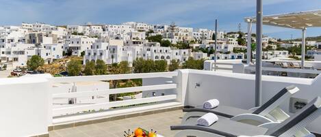 Una terrazza sul tetto con mobili bianchi, una ciotola di frutta e vista su edifici bianchi sullo sfondo.