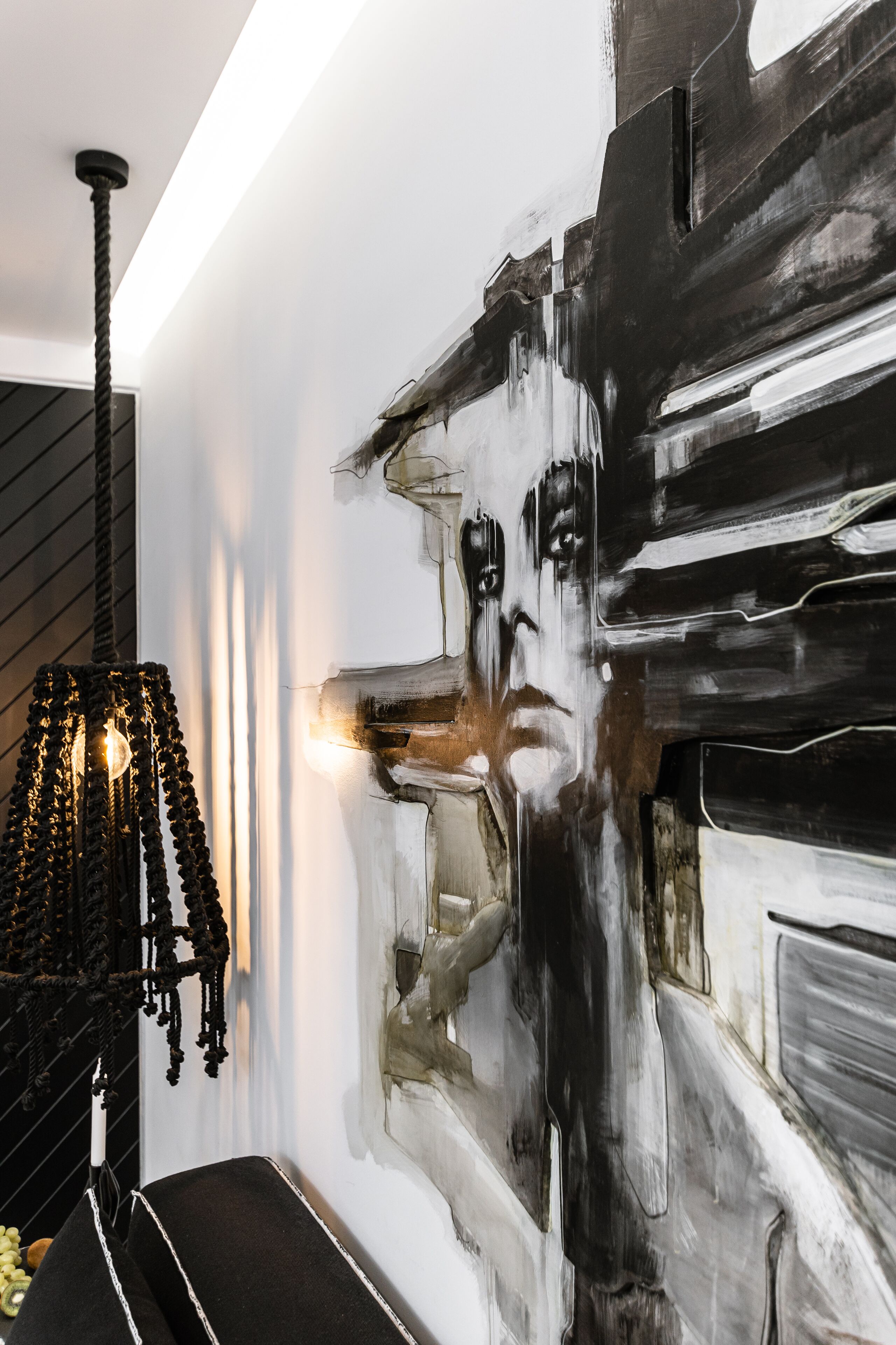 A modern interior with a black and white abstract painting on the wall, a black chandelier, and a black bench.