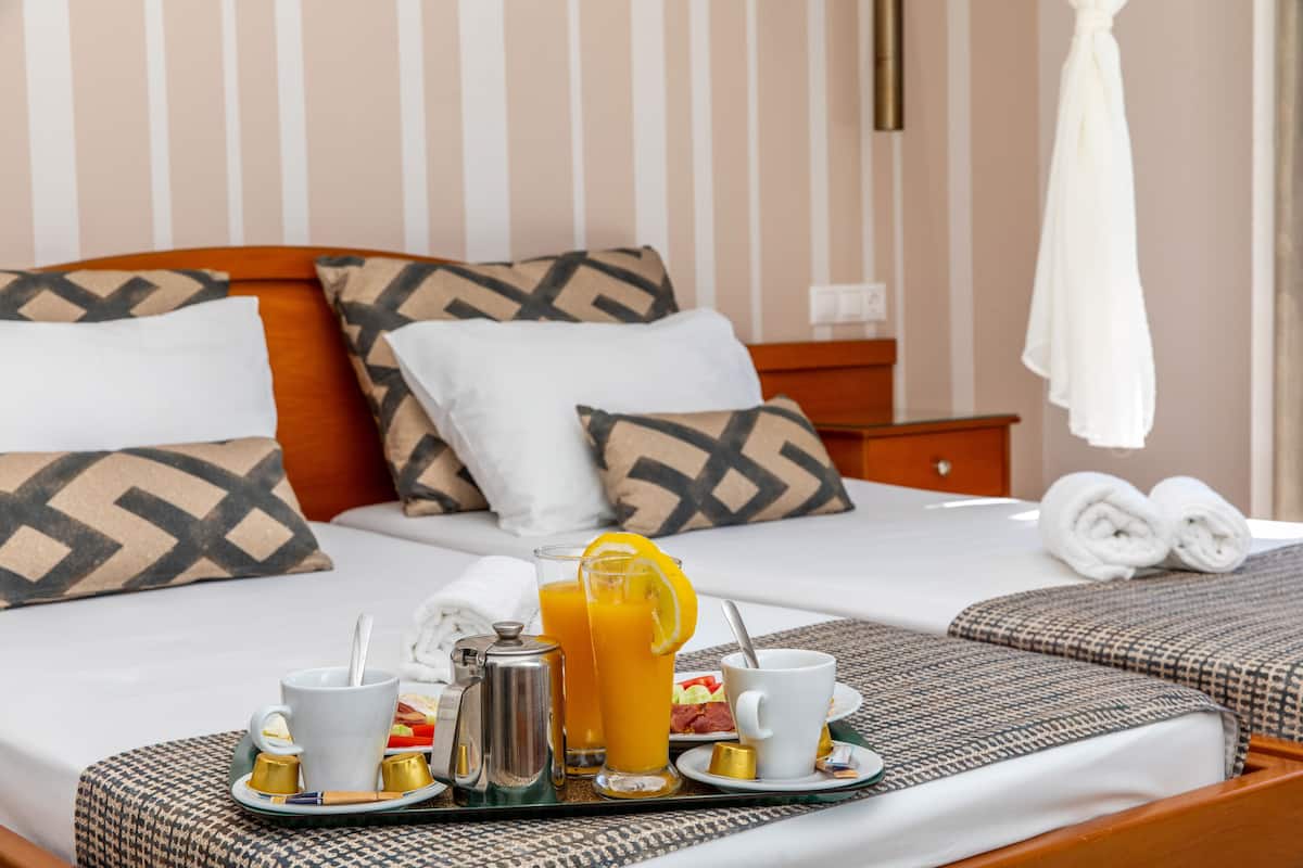 Quarto de hotel com uma cama bem arrumada, um tabuleiro com itens de café da manhã e uma mesa de cabeceira com abajur.