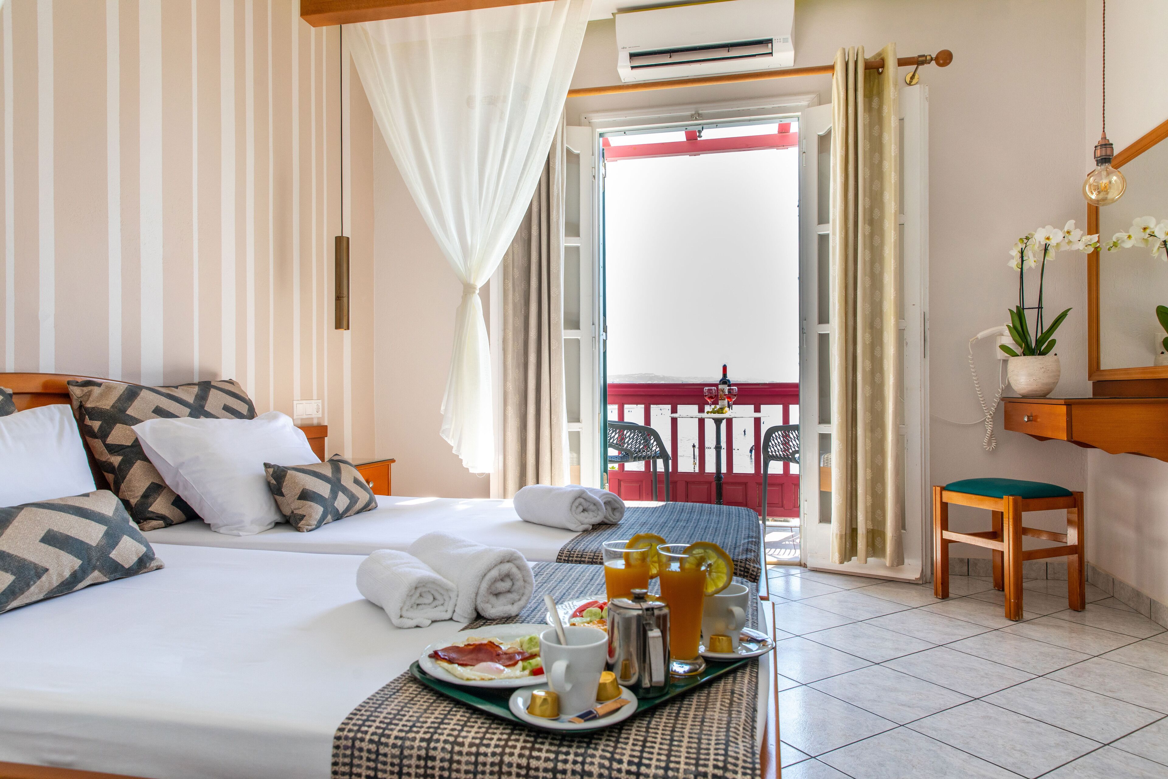 Habitación de hotel con cama, bandeja de desayuno y balcón con vistas.