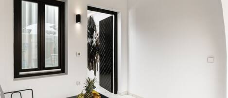 A modern room with a bed, a small table with fruits and a book, a window, and a door with a black geometric design.