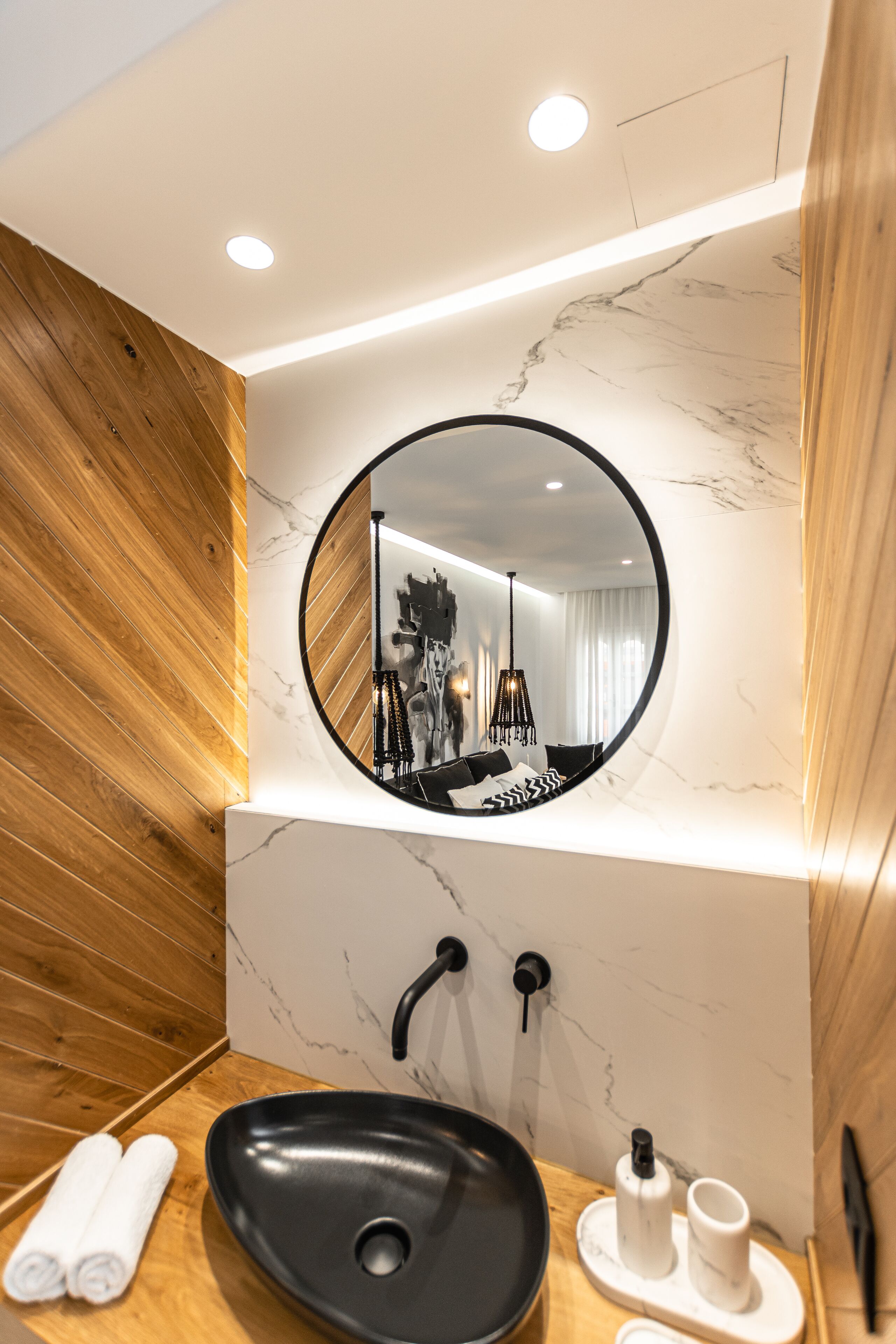 A modern bathroom with a round mirror, black sink, wooden paneling, and a marble wall.