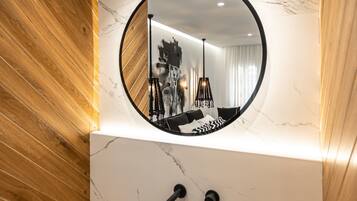 A modern bathroom with a round mirror, black sink, wooden paneling, and a marble wall.