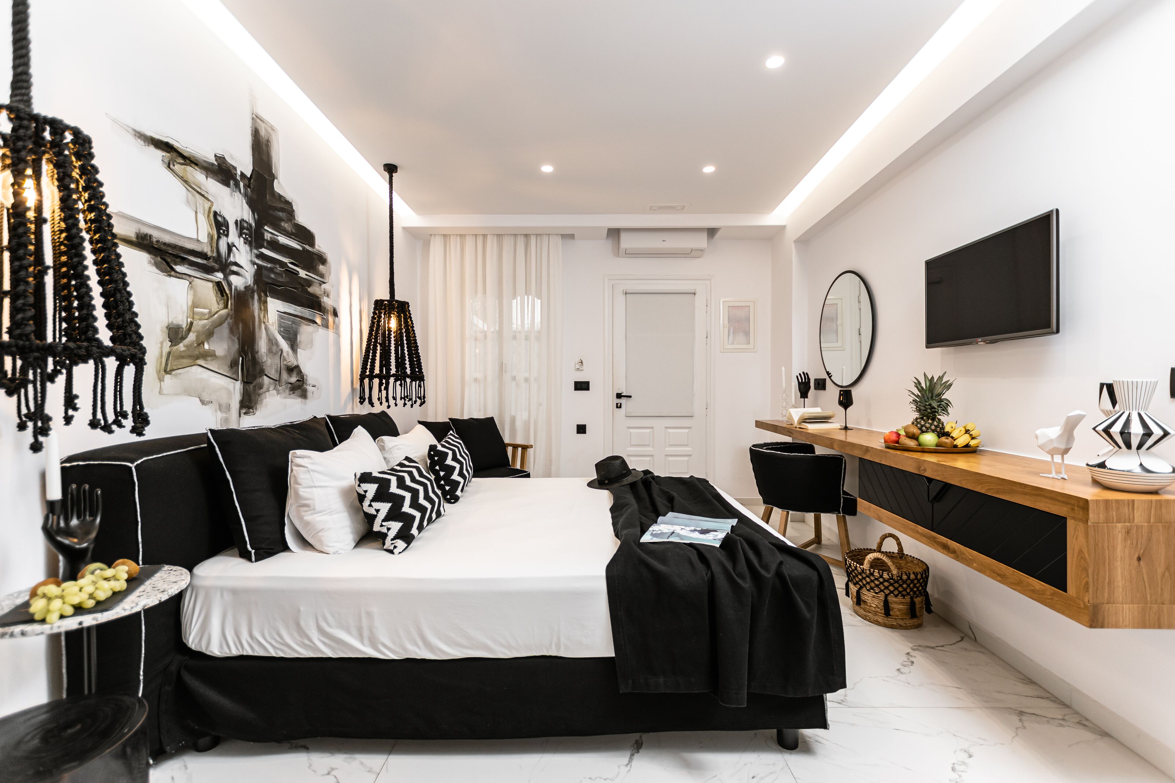 A modern bedroom with a black and white color scheme, a bed, bedside table, and a wooden console table with fruit.