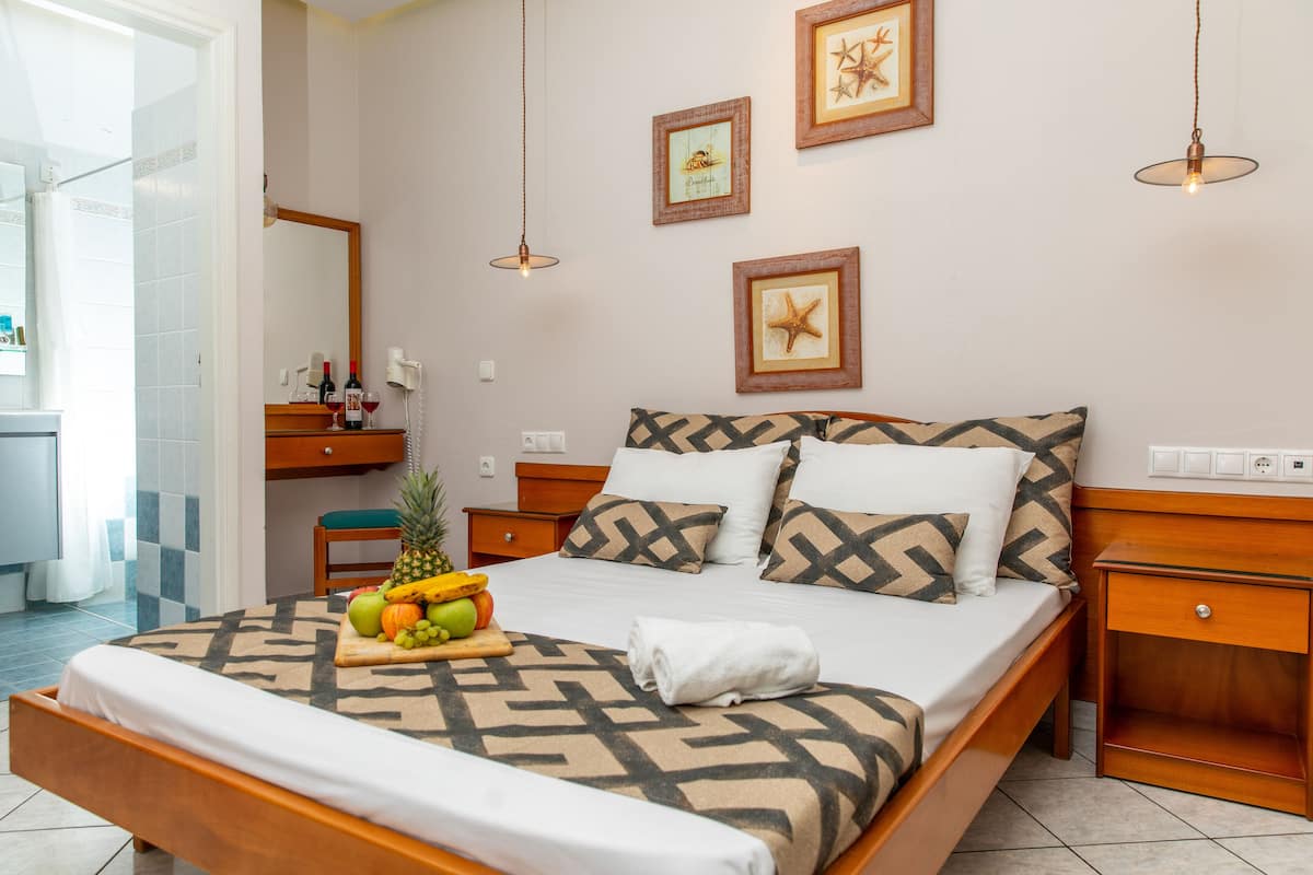 Cama bem arrumada com roupa de cama estampada, uma cesta de frutas sobre a cama e uma toalha dobrada no pé da cama.