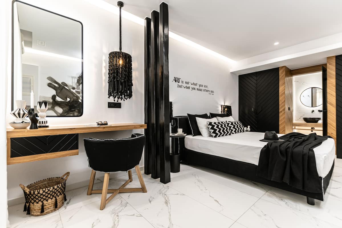 Quarto moderno com cama grande, escrivaninha, cadeira, espelho e obra de arte na parede.