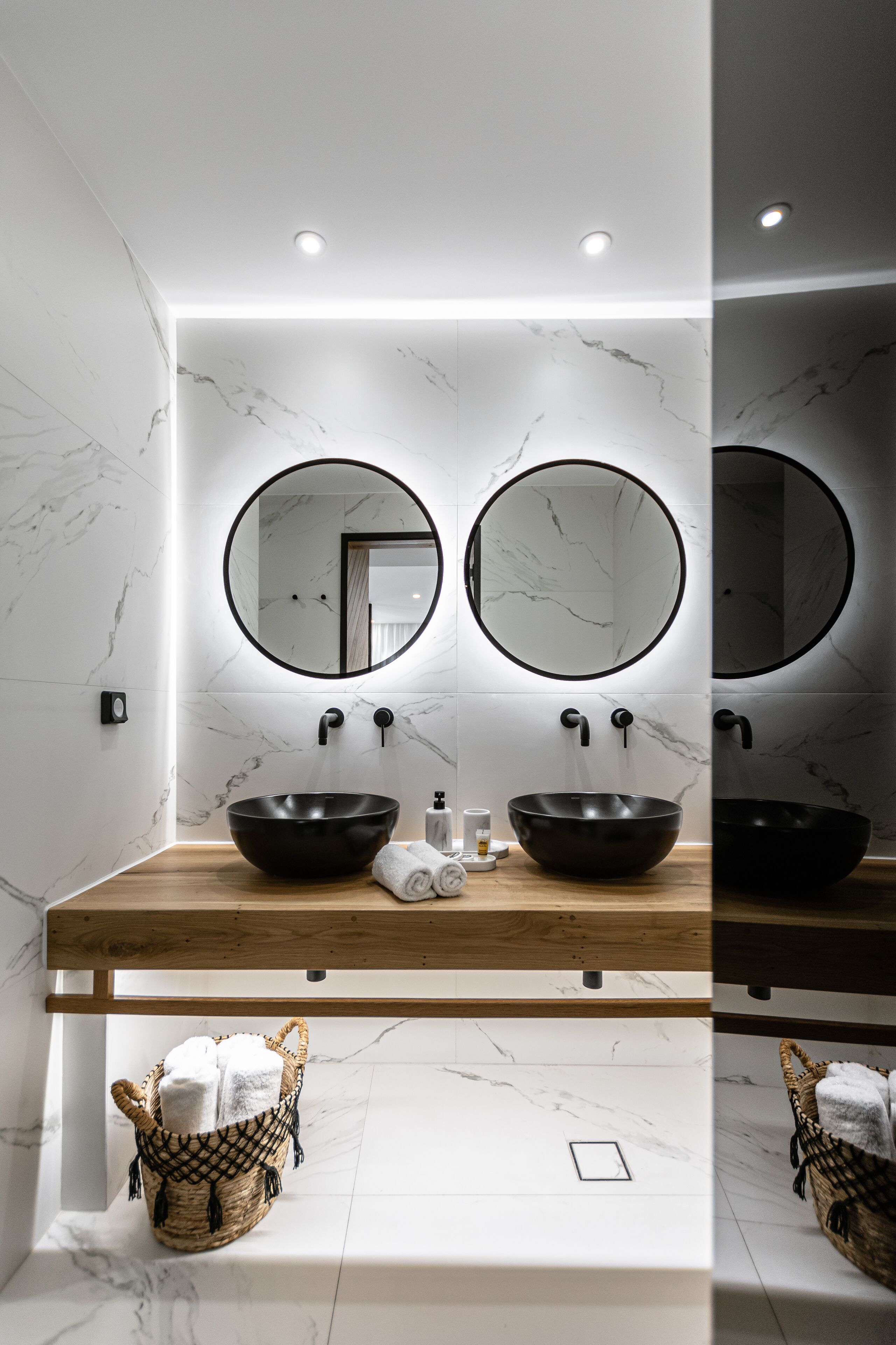 A bathroom with two round mirrors, a black vessel sink, and a wooden countertop.