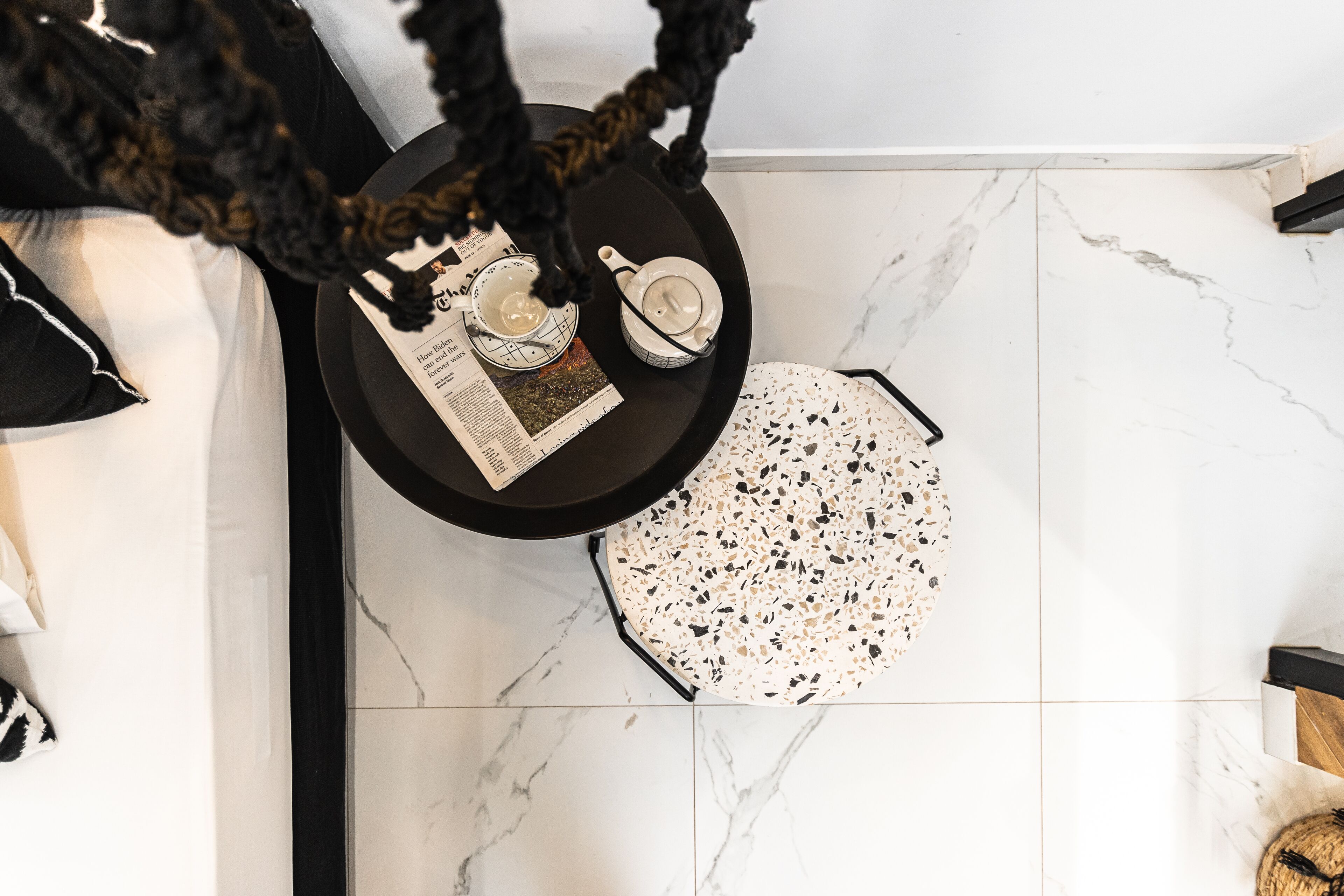 A room with a black round table, a white teapot, a cup, and a newspaper.