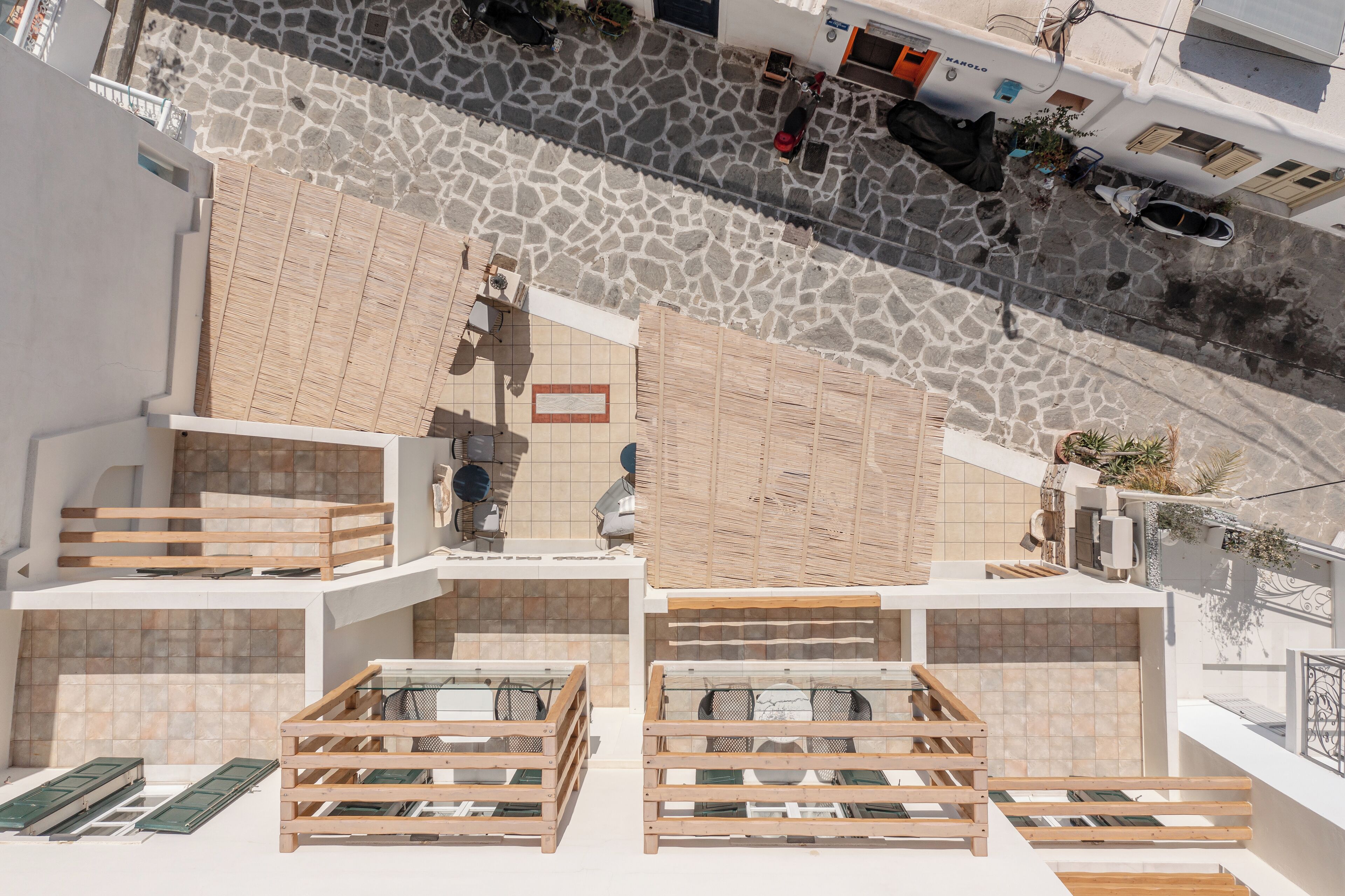 A rooftop terrace with multiple wooden seating areas and a stone-paved street below.