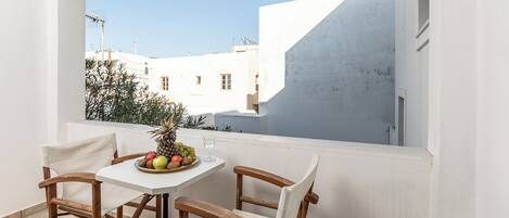 Un balcón con una mesa y sillas blancas, un frutero y una vista despejada de edificios y cielo.