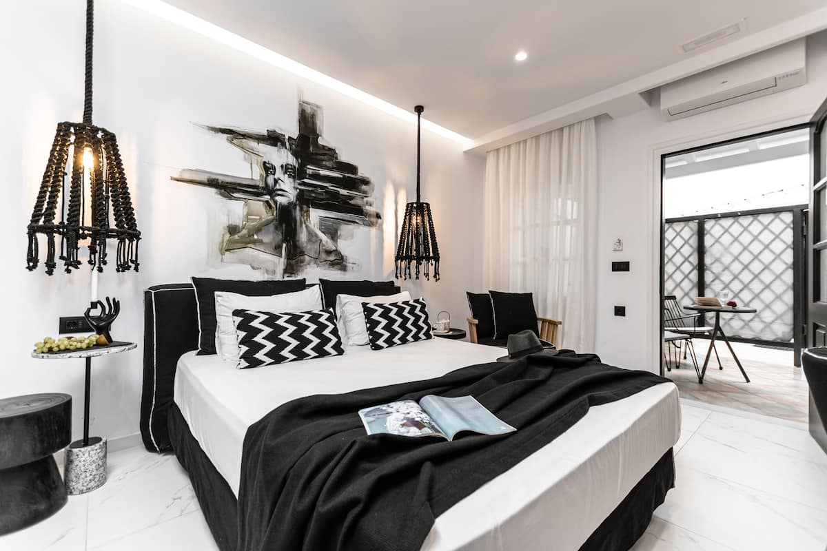 Quarto moderno com uma cama grande, roupa de cama preta e branca, um quadro abstrato em preto e branco na parede e uma varanda com vista.