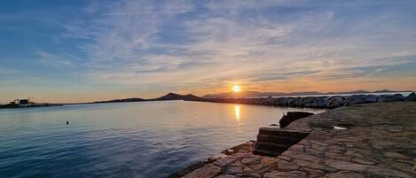 A sunset over a calm body of water with a stone pathway leading to a dock.