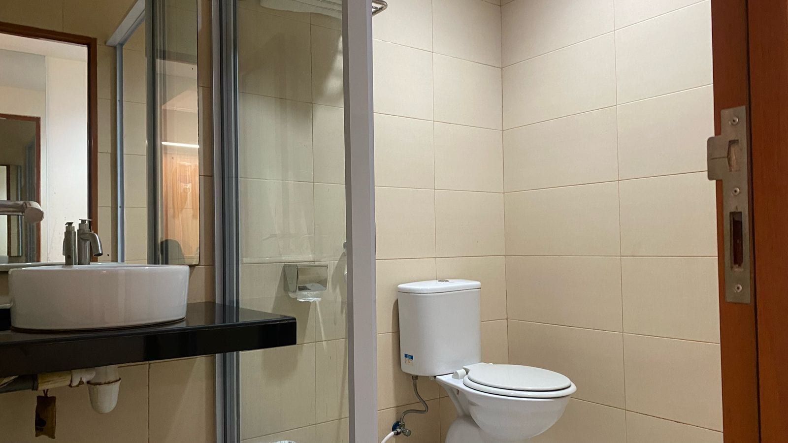 A bathroom with a white toilet, a white sink with a black countertop, and a glass shower enclosure.