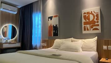 Et hotelværelse med en seng, et natbord med lampe, en vægmonteret aircondition og et vindue med gardiner.