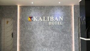A sign for the Kaliban Hotel with a marble wall background and a logo above the text. - Kaliban Hotel (Batam)