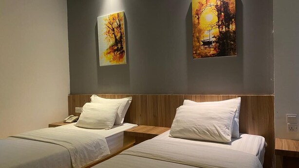 A hotel room with two single beds, a wooden headboard, and two paintings on the wall. - Kaliban Hotel (Batam)