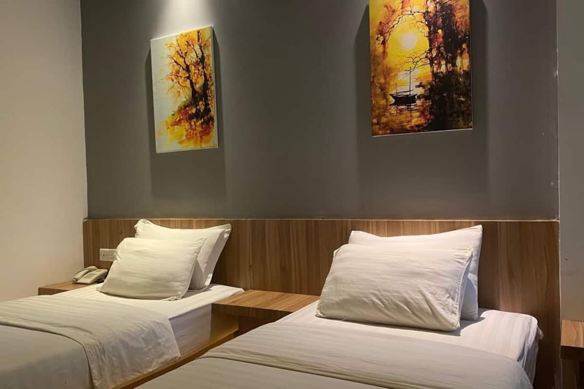 A hotel room with two single beds, a wooden headboard, and two paintings on the wall.