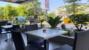An outdoor cafe with tables and chairs, potted plants, and a view of the street. - Kaliban Hotel (Batam)