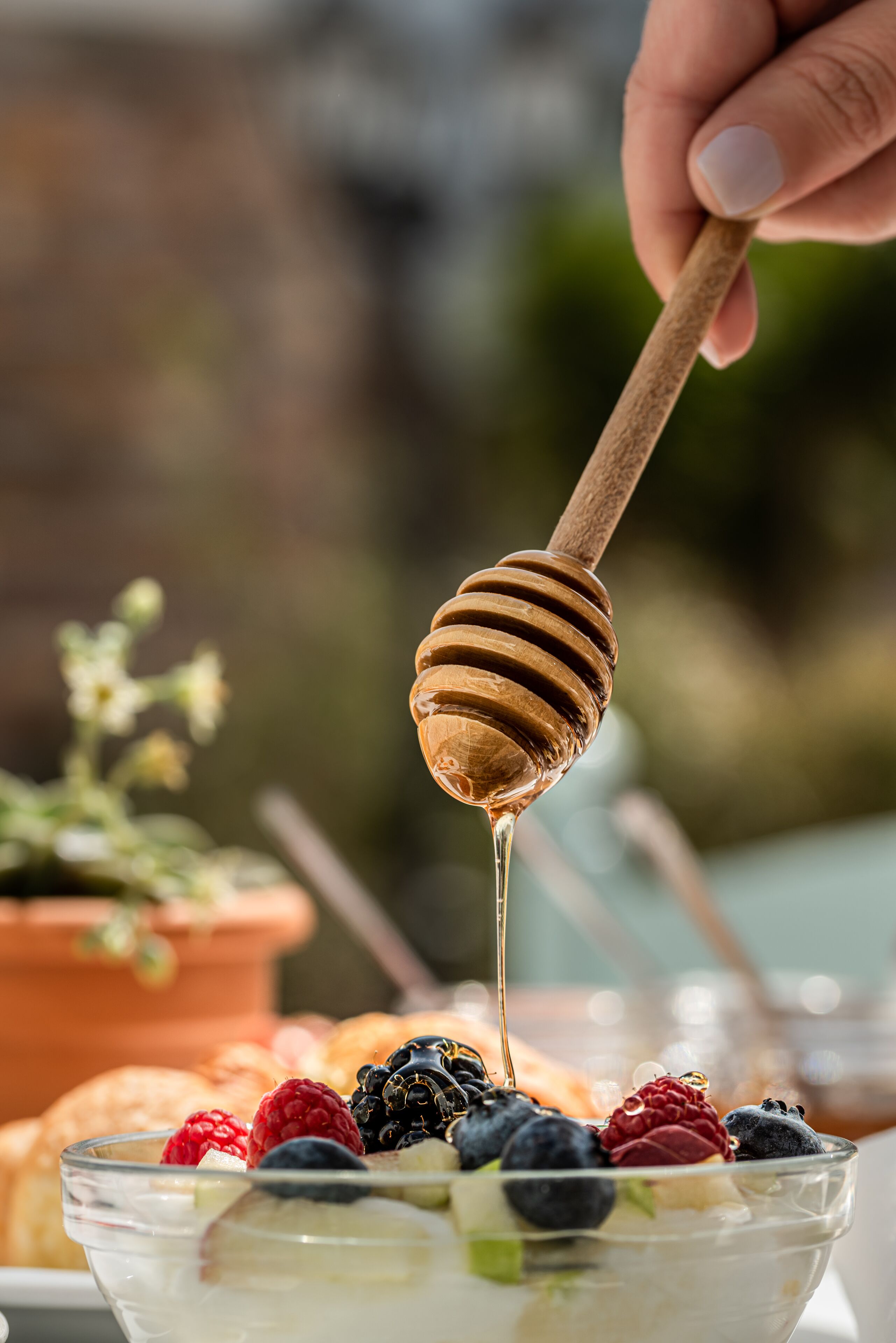 A hand holding a honey dipper dripping honey over a bowl of fruit and yogurt.
