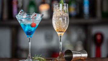 Two cocktails in martini glasses with ice and garnishes, and a cocktail shaker on a wooden surface.