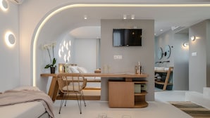 A modern, well-lit room with a wooden desk, a comfortable chair, a flat-screen TV, and a bed. - Argo Boutique Hotel (Naxos)