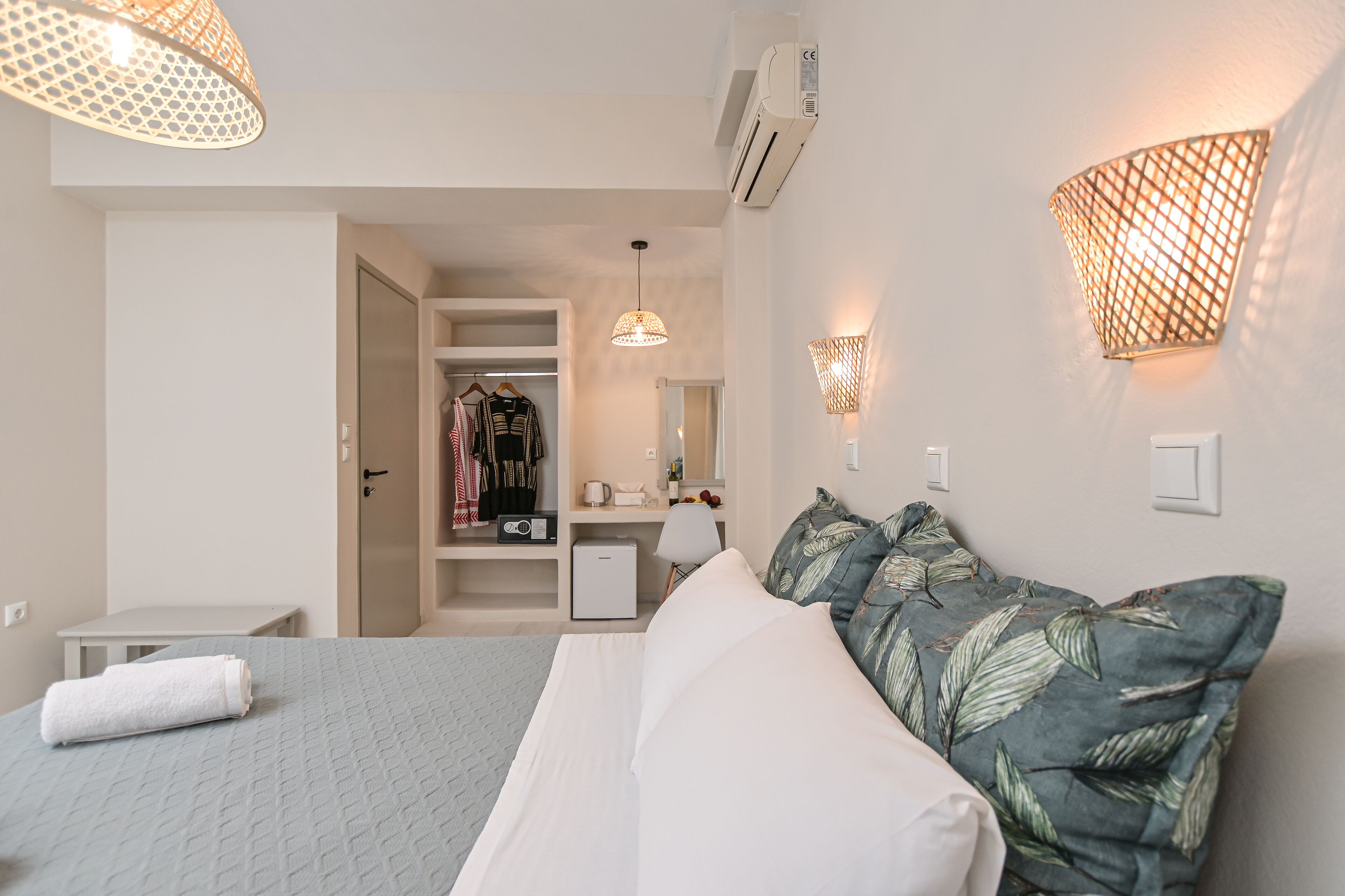 A hotel room with a bed, a bedside table, a wardrobe, a desk, and a mirror.