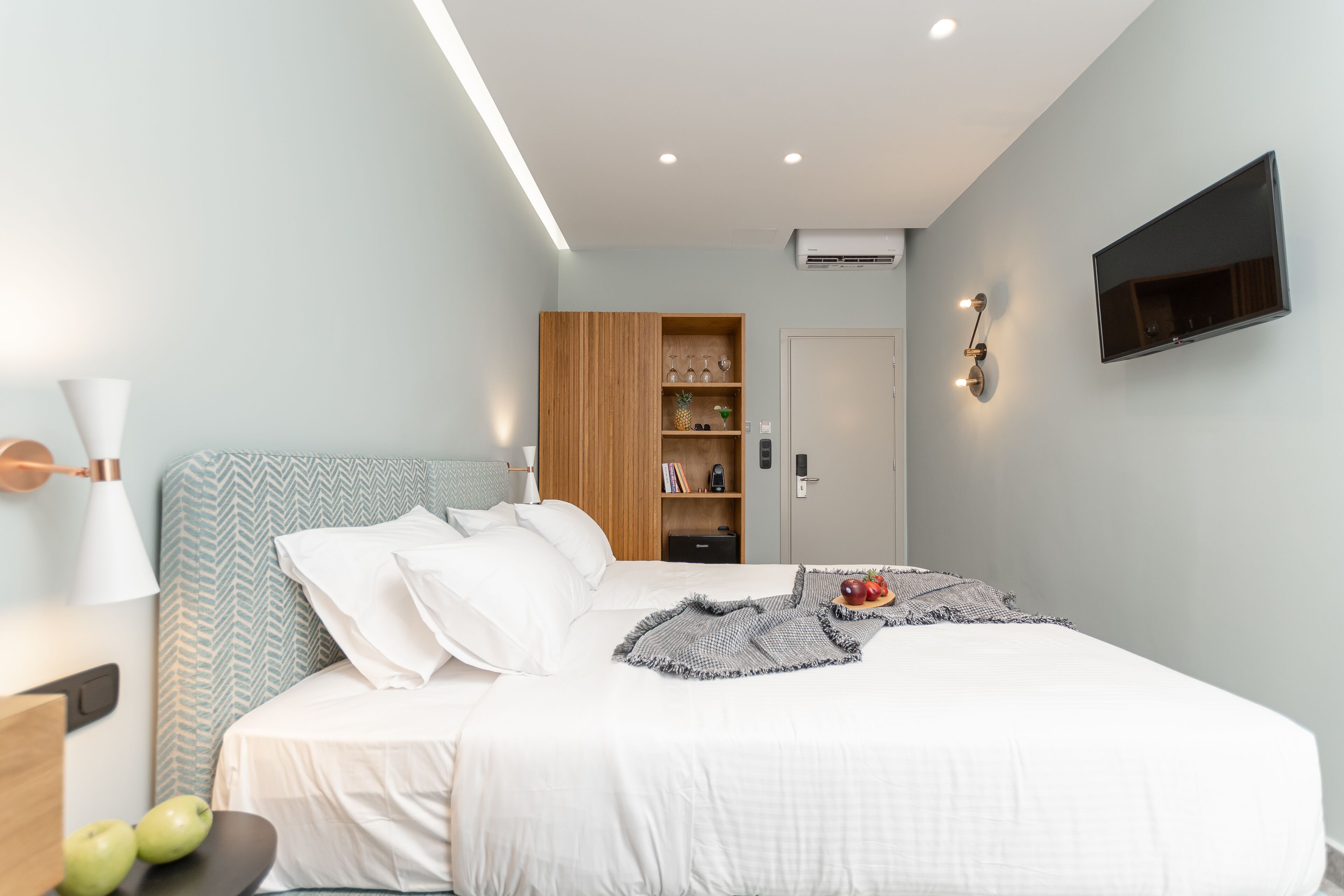 A modern bedroom with a bed, bedside table, lamp, wardrobe, and a mounted TV.