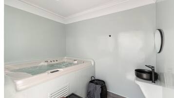 A modern bathroom with a large bathtub, a small sink, and a basket of fruits.
