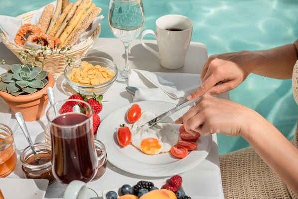 A breakfast setup by a pool with bread, fruit, and beverages.