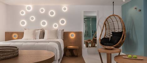 A modern bedroom with a bed, bedside tables, a hanging chair, and a small dining area.