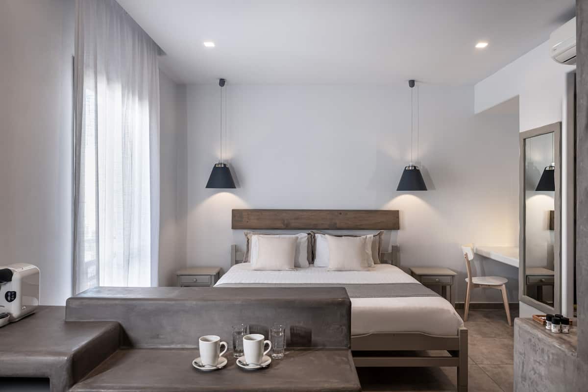 Moderni hotellihuone, jossa on suuri sänky, yöpöydät, oleskelualue ja suuri peili.
