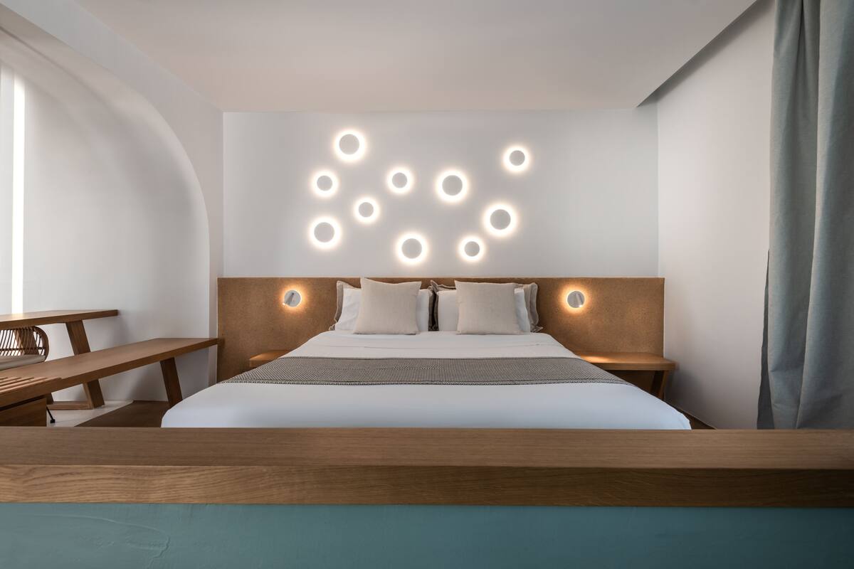 Moderni hotellihuone, jossa on puinen pääty, suuri sänky valkoisilla vuodevaatteilla ja penkki sängyn päädyssä.