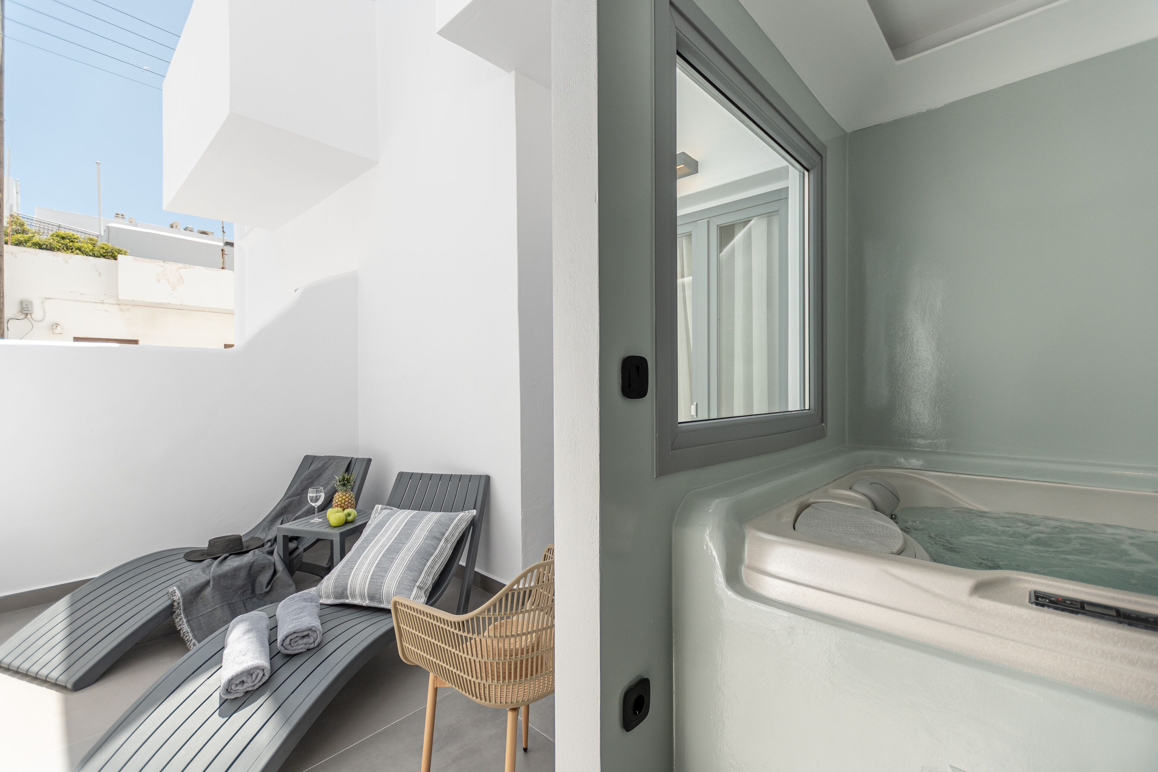 A modern bathroom with a bathtub, a sun lounger, and a small table with a pineapple and a glass.