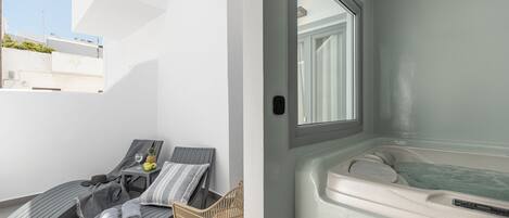 A modern bathroom with a bathtub, a sun lounger, and a small table with a pineapple and a glass.
