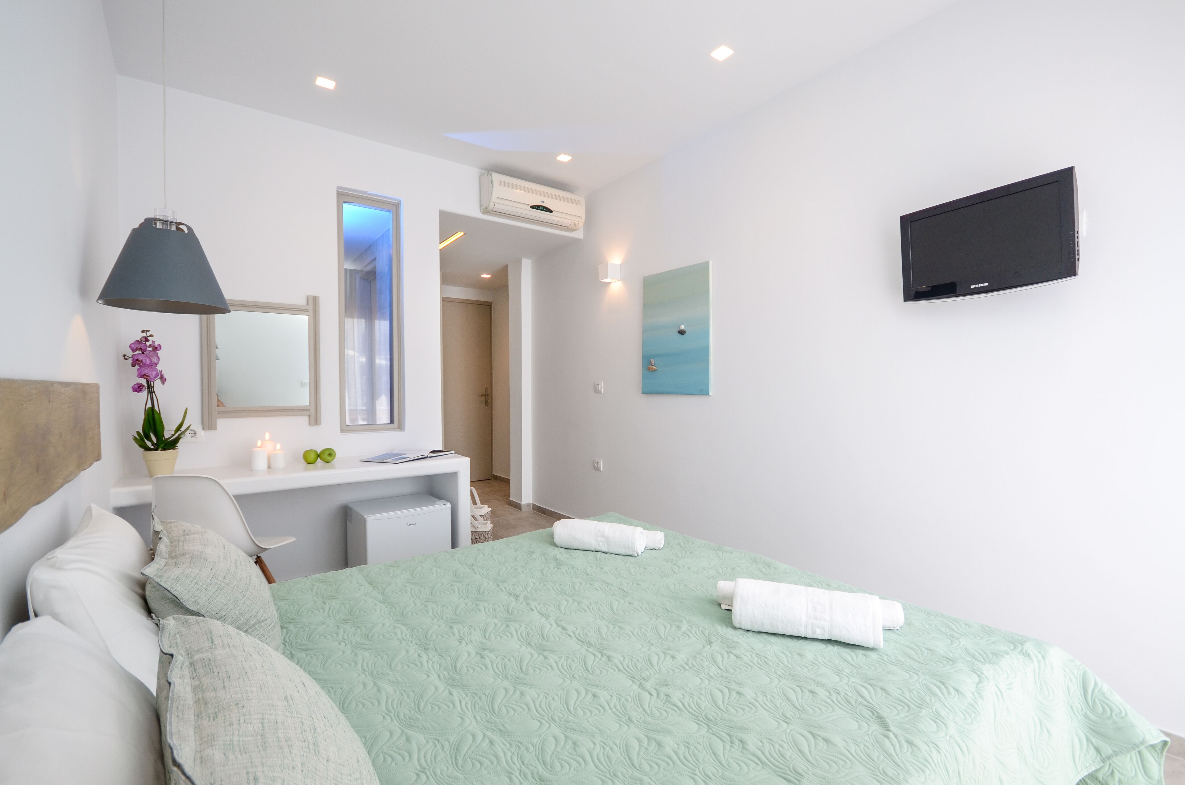 A modern hotel room with a bed, a desk, a chair, a TV, and a bathroom door.