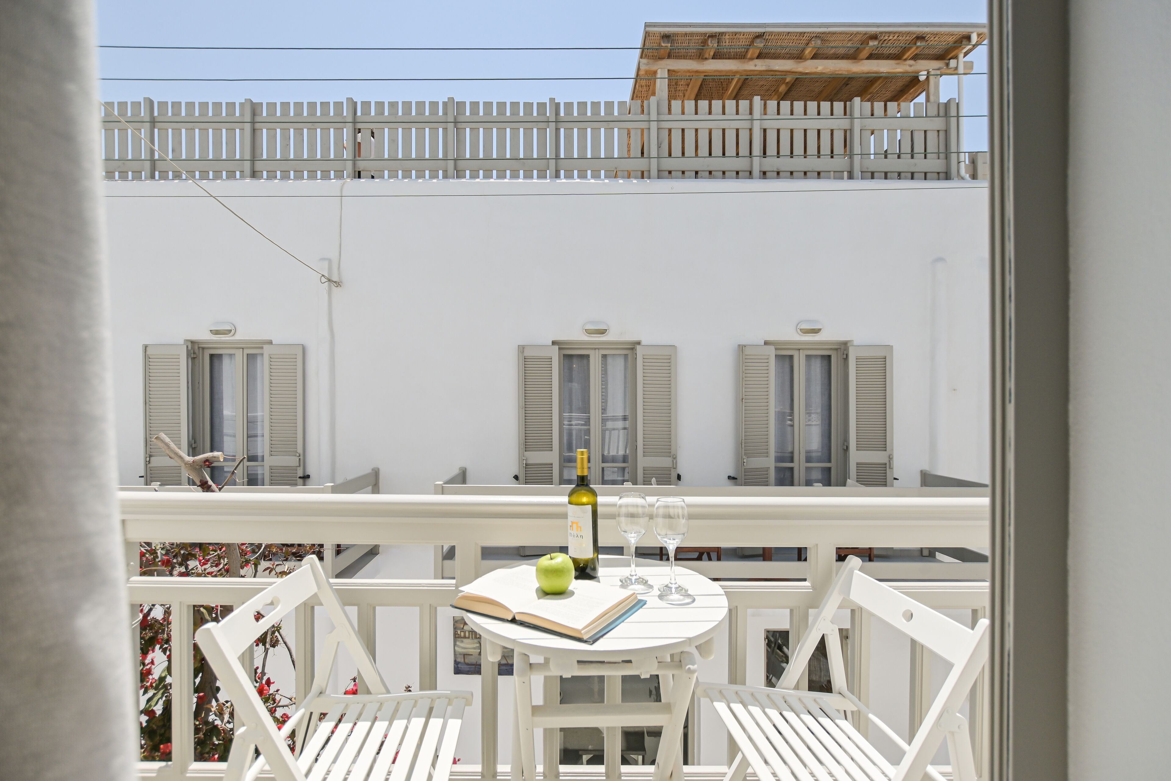 A balcony with a table, two chairs, a bottle of wine, two glasses, and an open book.