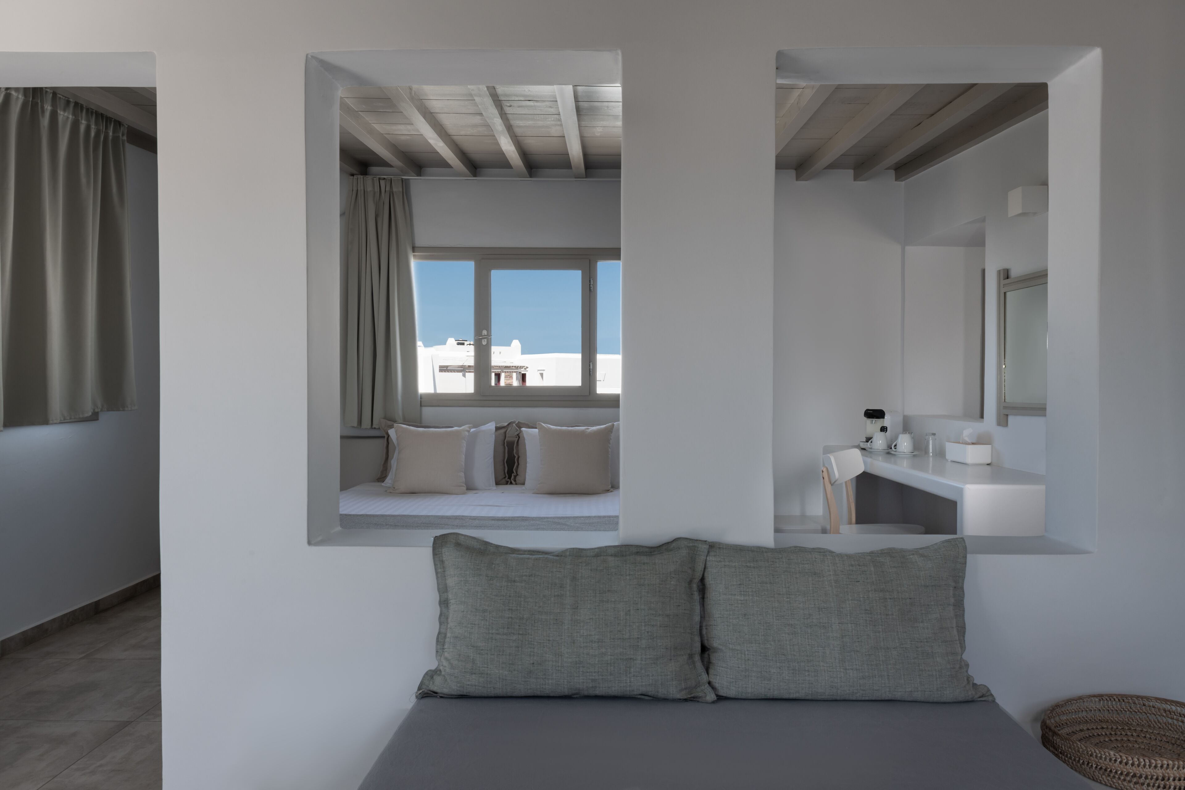 A modern bedroom with a large bed, a window seat with a view, and a bathroom with a mirror and sink.