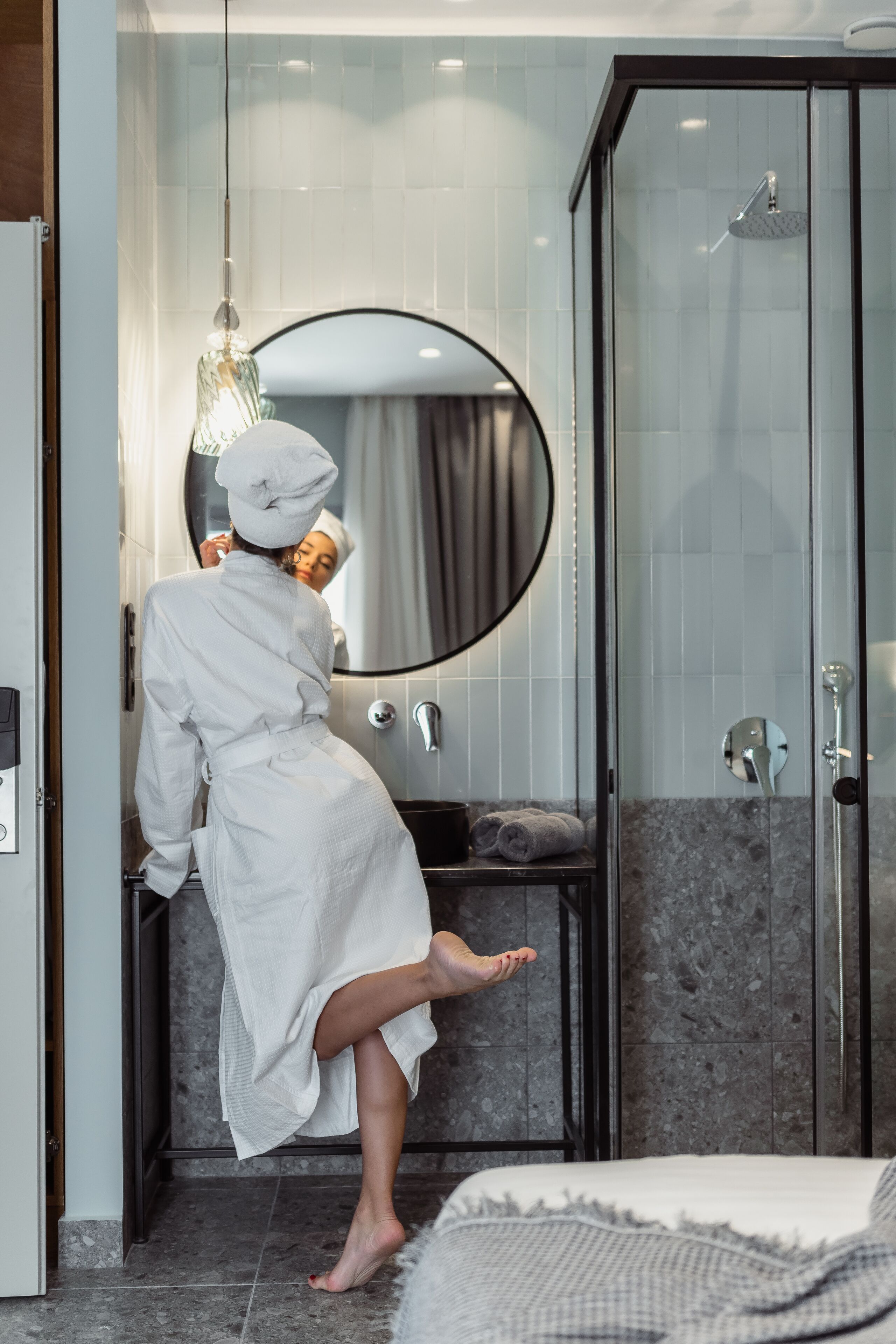 Un baño moderno con cabina de ducha de vidrio, un espejo redondo y un perchero para toallas.