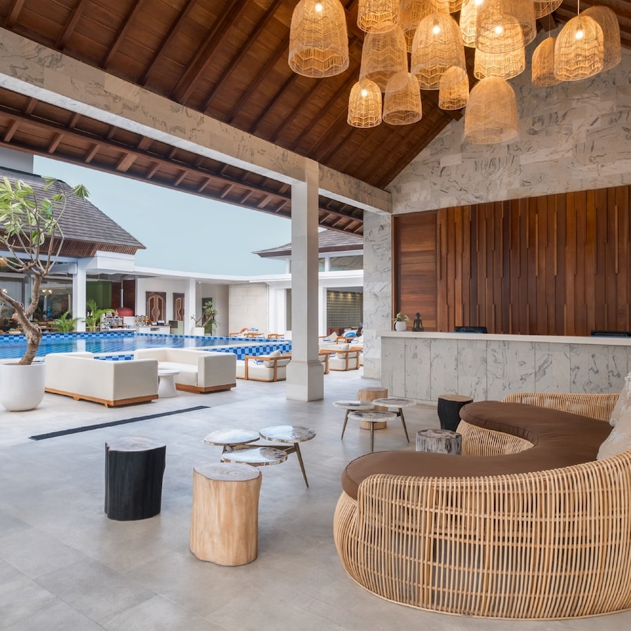 A spacious outdoor lounge area with a pool, comfortable seating, and a wooden ceiling.