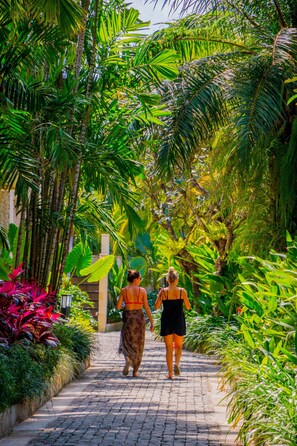 A pathway lined with lush green foliage and palm trees, leading towards a building. - Montigo Resorts Seminyak (Keroboken Kelod)