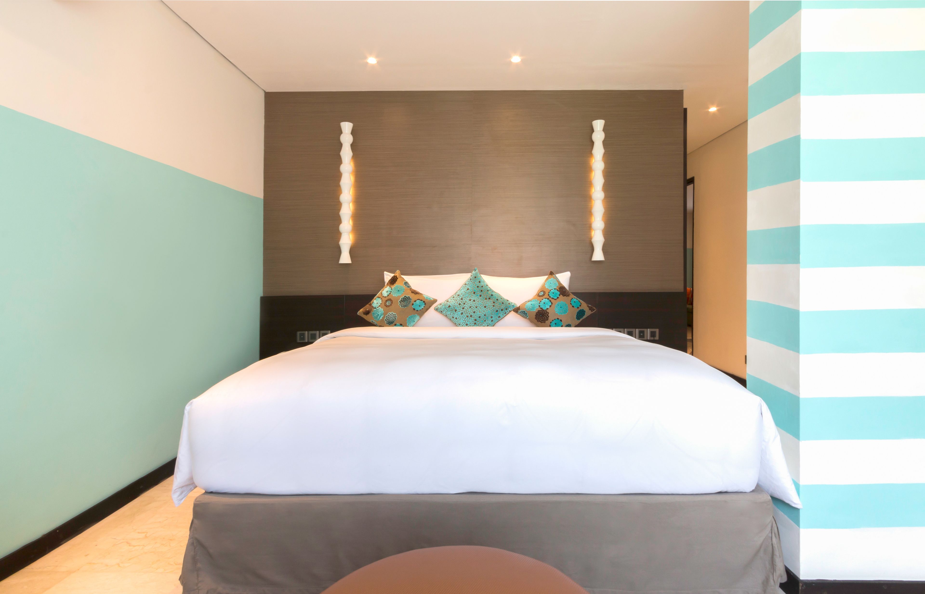 A modern hotel room with a large bed, a wooden headboard, and decorative wall sconces.