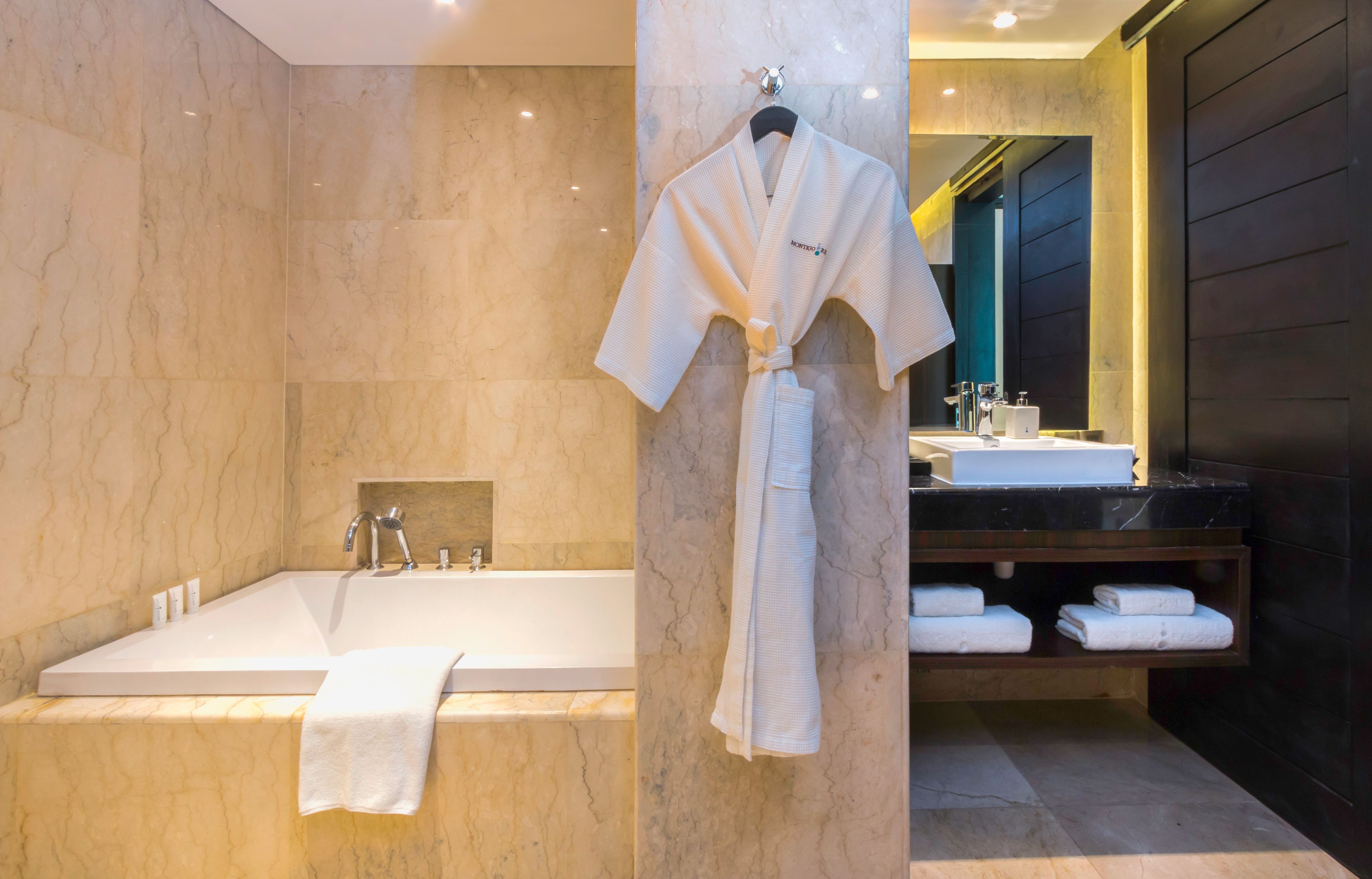 A modern bathroom with a large bathtub, a vanity with a mirror, and a robe hanging on a hook.